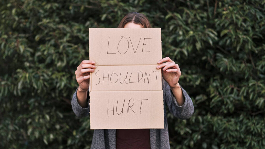 A woman holds a sign in front of her face that reads, "Love shouldn't hurt."